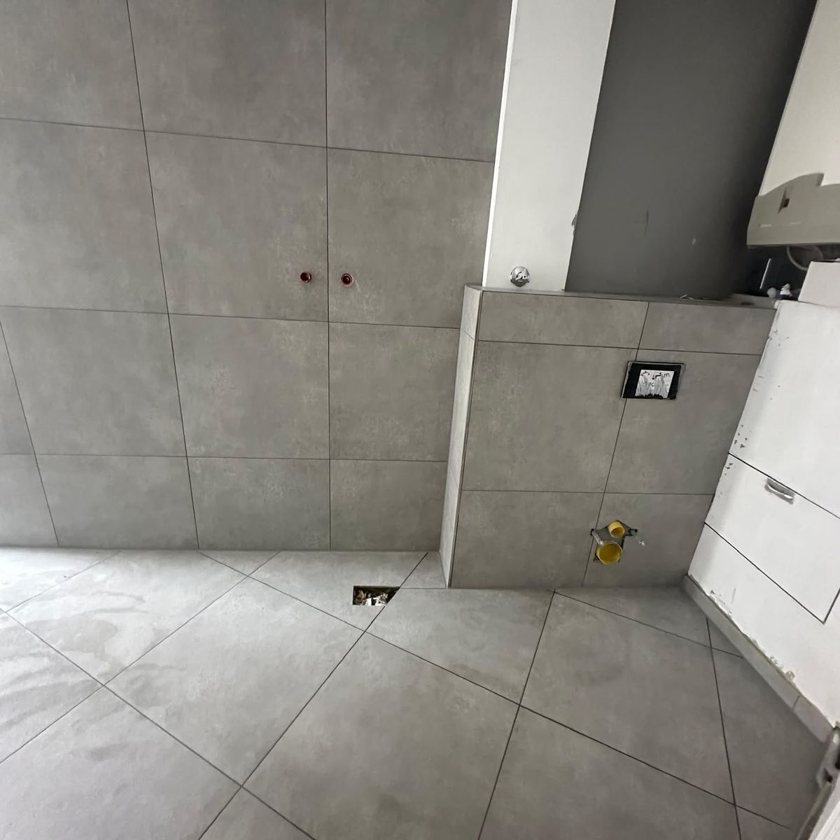 Bad mit grauen Großformatfliesen an Wand und Boden und gefliester Vorwand für das wandhängende WC